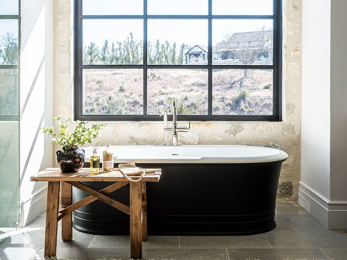 Free standing bathrub with black exterior in front of a window