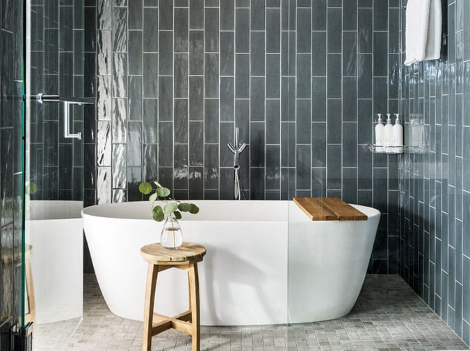 White free standing bathtub in front of a grey tile wall